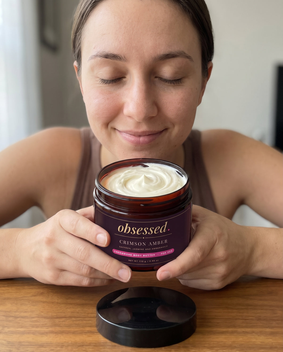 A woman holds the open Crimson Amber jar close to her face and smells it
