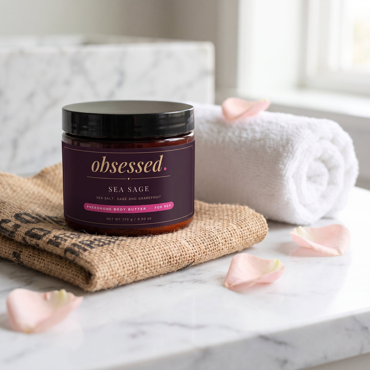 The Sea Sage jar on a marble vanity with a folded coffee sack and rose petals