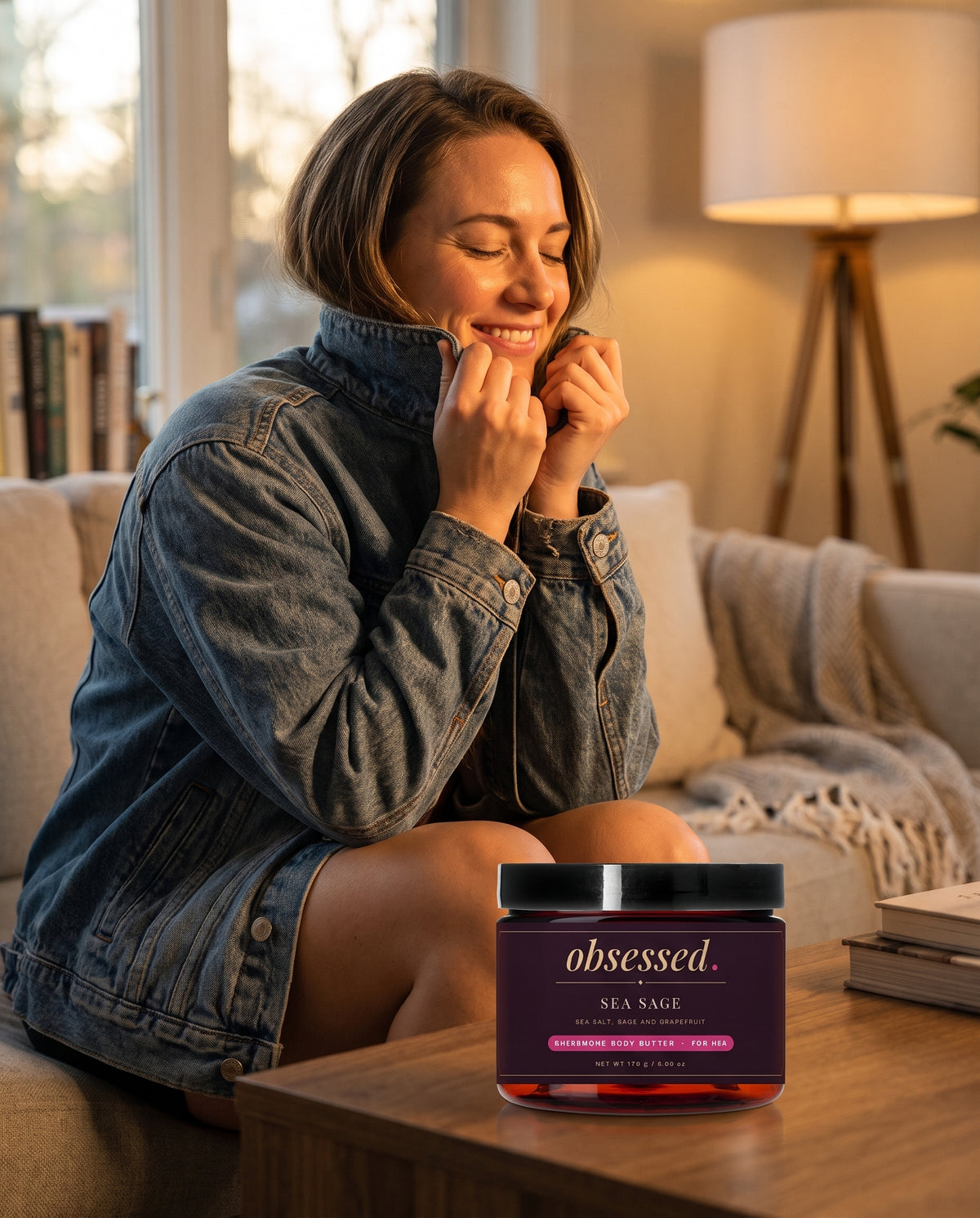 A woman in an oversized jacket breathes in the collar, the Sea Sage jar on the table